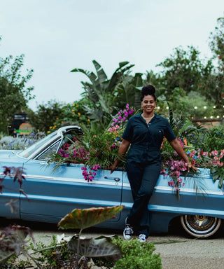 Black woman in front of a flower installation in a low rider car